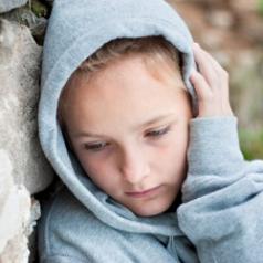 Unhappy, solitary child leans against brick wall