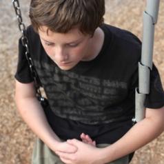 A lonely adolescent boy sits on a swing