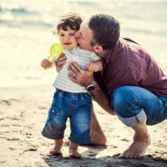 A father hugs and kisses his toddler on the beach