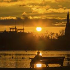 Silhouette of man sitting on a park bench at sunset