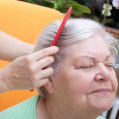 A senior smiles as a caregiver combs her hair.