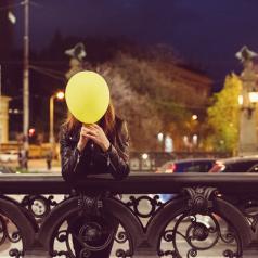 Person stands at bridge holding balloon in front of face