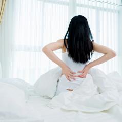 Rear view photo of person with long black hair waking up with hands on back in pain