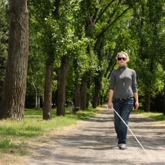 A blind woman walks through a park