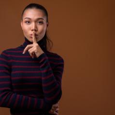 Person in turtleneck with long ponytail holds finger to lips
