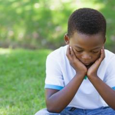 A young black boy in a park looks glum
