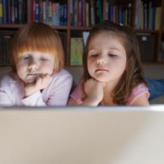 Young girls (5-6) lying on floor using laptop,  contemplating with hand on chin
