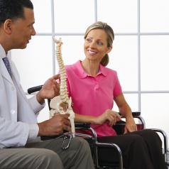 Doctor shows a spinal model to a woman in a wheelchair