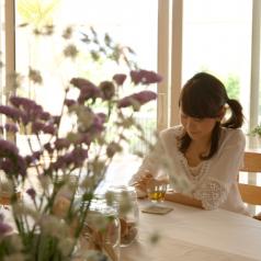 Woman with cup of tea, sitting at table in home, flowers in foreground