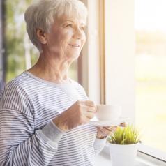 An elderly woman drinks coffee at her window
