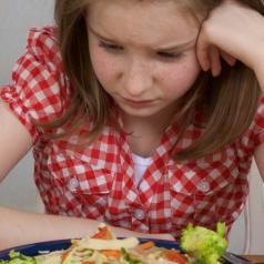 Young girl looks down sadly at plate of food