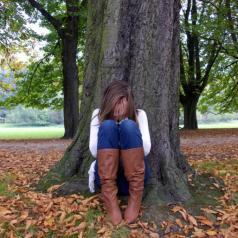 Young woman leaning against a tree with head in hands