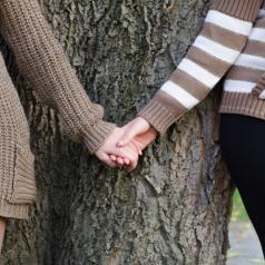 Same-sex couple holding hands against a tree
