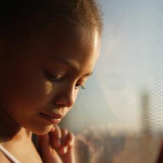 Sad young girl leaning next to a window