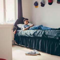 Teenage boy lying on his bed at home using a smartphone to text
