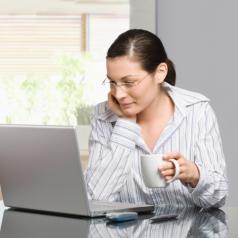 Woman holding mug and working with laptop
