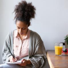 Young woman sitting at table writing in notepad