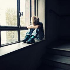 Young child sitting alone in window with head down 