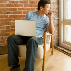 Young man with laptop looks lost in thought