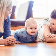 Two mothers smiling at baby on wood floor