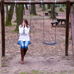 Woman sitting on a swing and covering her face