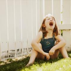 Young child sits in grass by fence and screams