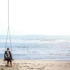 Woman sitting on beach swing facing the sea