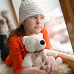 Adolescent girl holding teddy bear looks out window