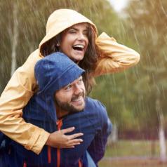 Smiling man carries laughing woman on his back through rain