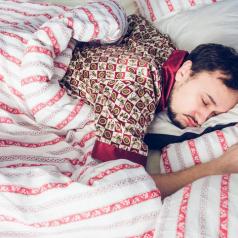 Man sleeping under striped comforter in silk pajamas