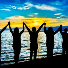 Group of people on beach at sunset raising linked hands to sky