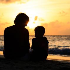 parent and child looking at sunset on beach