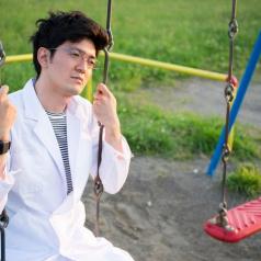 Person in white lab coat sits on swing looking thoughtful