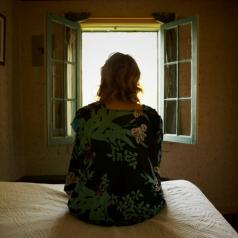 Person seated on bed looks out open window