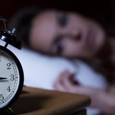 Close-up of alarm clock on night table, blurred person in bed awake