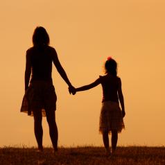 Rear view of mother and daughter hold hands at sunset
