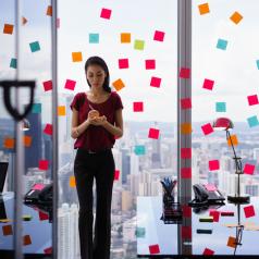 Office worker stands by glass wall covered with sticky notes writing something on list