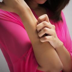 Shoulder and torso view of a person scratching their arm. The person is wearing a magenta top and has shoulder-length hair.