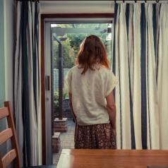 Rear view of person standing by curtains of French doors and looking out