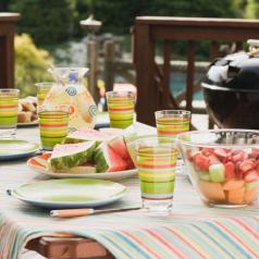 Fresh fruit, lemonade, place settings, and barbecue grill spread across picnic table