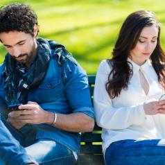 Two people sitting on a bench face away from each other, both using their phones