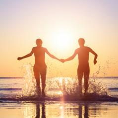 Rear view of a couple holding hands and splashing in waves at beach