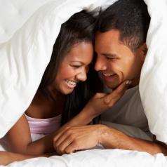 Couple smiles at each other with faces close together under duvet cover