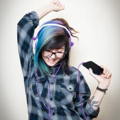 Young adult with headphones and brightly dyed hair listens to music