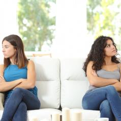 Sisters seated at opposite ends of sofa, arms crossed, looking away from each other