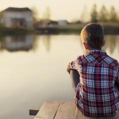 Boy sitting alone on dock overlooking lake