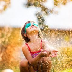 Young child in goggles plays in sprinkler with carefree smile