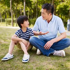 A father sits with child on the grass as the two talk seriously