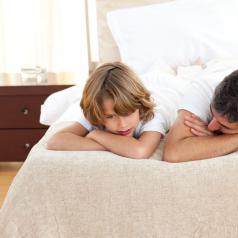 Father and adolescent child lie on bed, heads on their arms, having a conversation