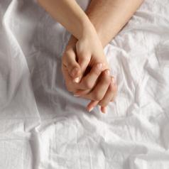 Close-up shot of forearm and hands of couple on white sheet